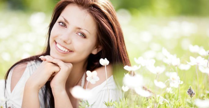 Woman sitting in a field of flowers smiling with her head resting on her hands