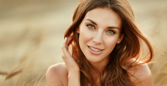 Woman with glowing skin and flowing brown hair outdoors