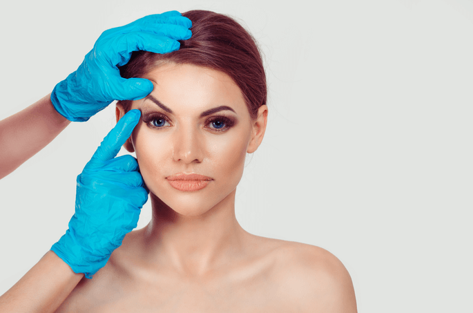Surgeon's gloved hands examining a woman's eyes and eyelids prior to cosmetic eyelid surgery