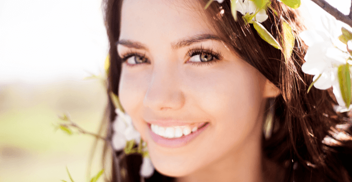 Young brunette woman smiling outside alongside white flowers