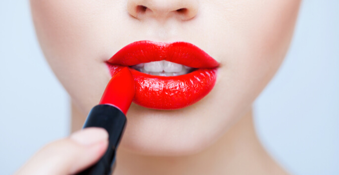 Woman applying red lipstick to her plump lips