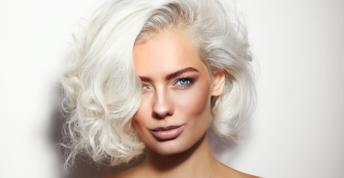 Woman with a short, platinum blonde bob and taut cheekbones pursing her lips