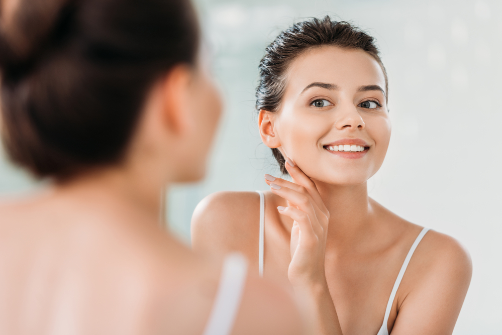 Smiling woman with bright, clear skin looking in the mirror and gently touching her face