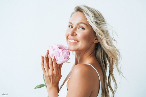 Mature blonde-haired woman smiling while holding a pink flower