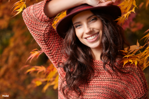 Woman with long brown hair wearing a red sweater and red hat outside among fall leaves