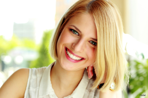 Joyful woman with a blonde bob resting her head on her hand and smiling