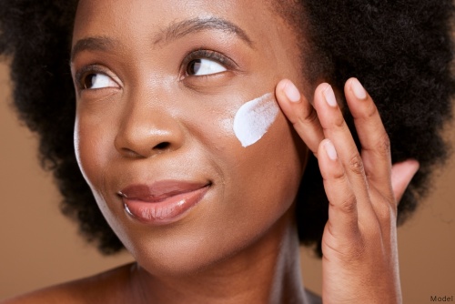 Woman softly smiling while applying a skin care product to her cheek